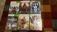 Six Xbox 360 games laid out on a patterned surface, showing cover art and titles clearly.
