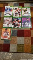 Seven Xbox sports game cases including NHL 12, 13, 15, 16, 18, 20 and Madden 20, displayed on a multi-colored carpet.