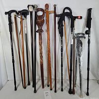 Full view of multiple walking sticks and canes standing upright showing variety of wood and metal materials