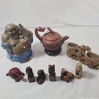 Full view of the lot items arranged on a white surface showing Buddha figurine, teapot, carved cups, bull figurine, and smaller statues