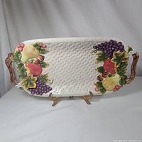 Full view of the Cornucopia Collection serving tray on a stand showing detailed fruit and grape cluster designs and woven textured surface.