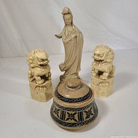 Set of three carved Chinese figurines and one ceramic container on white backdrop.