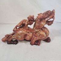Full side view of orange maroon stone carved dragon showing its raised head, expressive face, and detailed claws.