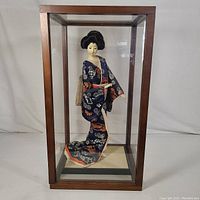 Full view of the Geisha doll inside the wood and glass display case showing the front and base