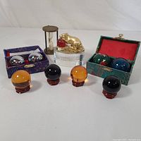 Full display of the lot showing 4 spheres on stands, 2 Baoding ball sets in decorative boxes, hourglass timer, and gold Naga with red gemstone on crystal block.