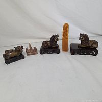 Front view of all five stone figurines on wooden stands showing varying stone types and sizes, including lions and seal shaped figures.