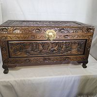Front view of trunk showing high relief carved scenes of Chinese junks and floral border.
