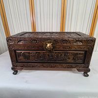Front view of the wood carved cedar trunk chest showing detailed ship carving and floral border with metal latch.