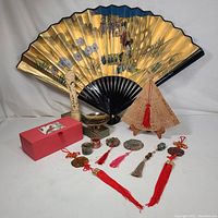 Photo showing the large vintage Chinese hand painted fan along with multiple carved pendants with tassels, a small decorative bowl, a carved figurine, a decorative box, and a carved decorative fan on stand.