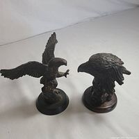 Two cast iron sculptures shown together: an eagle hawk statue with wings spread and a separate eagle head bust sculpture.