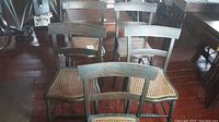 Five wooden antique dining chairs arranged close together. Chairs have cane seats and dark wood frames with a horizontal backrest.