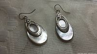 Front view of the pair of 925 sterling silver and mother of pearl drop earrings on fabric background.