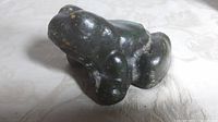 Front angled view of antique cast iron green frog doorstop on patterned fabric surface.