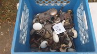 Blue crate filled with assorted antique door knobs and hardware pieces outdoors on grass.