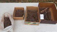 Four containers on a table holding various sizes of antique hand forged rosehead nails, visibly rusted with distinct rosehead shapes.