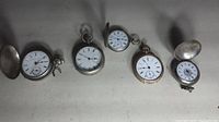 Five pocket watches laid out on flat surface