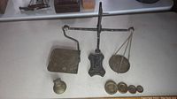 Full view of antique post office scale with cast iron base, balance arm, brass pan and weighing platform with five brass weights arranged in front.
