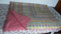 Quilt folded back showing front diamond patchwork and solid pink backing on printed sheet