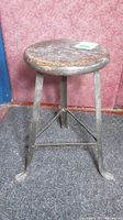 Front angle view showing the whole stool - round wooden seat and metal tripod base with curved feet.