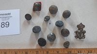 Full view of all 11 military buttons including a silver crown and monogram button, multiple round metal buttons with military insignia, and a red backing star-shaped badge.