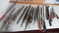Wide view of assorted hand files with wooden and plastic handles spread out on white surface.