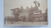 Photo showing the damaged steam locomotive and train cars with people standing around the wreckage.