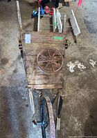 Top view of antique wooden wheelbarrow with metal spoked wheel attached and extra wheel on bed, displaying condition and structure.