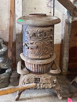 Frontal view of the round cast iron stove showing ornate scrollwork, door latch, circular top, and curved legs.