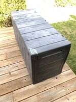 Side angle view of rectangular plastic deck box with wood grain finish showing broken hinge.