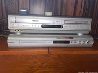 Front view of Toshiba DVD player on top of Philips DVD player showing both devices stacked and front panels visible.