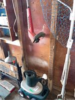 Photo showing the Toro 12 electric cut trimmer hanging on the wall, the plastic watering can on the floor, and part of the wheeled garden stool visible.