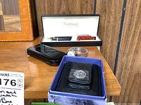 Overall shot showing all items including pen and pencil set in box, wristwatch, flip phone, money clip and card holder