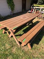 Brown wooden picnic table and benches outside on grass near house and bicycles