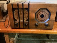 Front view of radio showing speaker grille on left with vertical wood slats and tuning dial with three knobs on right side