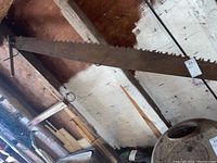 Photo showing entire crosscut saw hanging with one handle missing and rust on the metal blade.