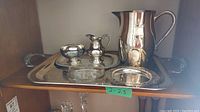 Photo showing the full set on shelf including large metal pitcher, Marlboro e.p. copper creamer and sugar bowl on tray, glass butter dish with silver plate underplate, and a silver plate tray.