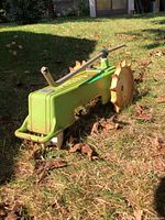Metal lawn sprinkler shaped like a tractor with two spiked wheels and spray arm, photographed on grass outdoors.