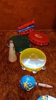 Full lot showing three plastic tambourines (red, green, yellow), two red clappers, white straight mute, and two blue wooden maracas with aquatic designs.