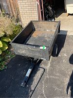 Full view of black Agro-Fab utility trailer showing bed and hitch arm, parked on driveway with garage and yard in background.