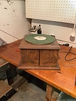Full front view of the Victor Talking Machine phonograph on a wooden table showing its wooden casing and green felt turntable.