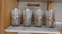 Full set of 8 vintage glasses in metal caddy with wood handle shown from front