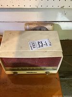 Front and top view of RCA Victor vintage radio with white casing and red speaker grill, showing tuning knobs and dial.