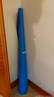 Blue vinyl material roll leaning against wall in corner, standing upright.