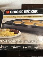 Box front showing Black & Decker branding and image of the griddle cooking pancakes and breakfast items, highlighting 8 serving capacity and nonstick coating.