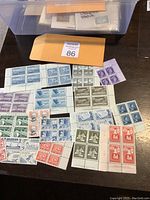 Image of assorted Canadian mint corner block stamps in various denominations and colors on a table with an envelope and storage box in background.