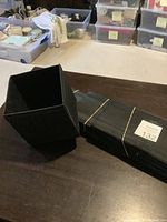 Photo of rectangular black foldable storage box secured with elastic band lying on table alongside open square black box.
