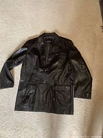Front view of the black leather coat laid flat showing full front details including sleeves, lapels, buttons, and pockets.