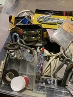 Overview of various household maintenance items including metal hooks, hinges, a roll of electrical tape, plastic containers with screws, and electrical cords.