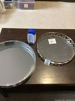 Two round mirrored trays on dark wood table with a bottle of lotion between them