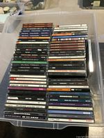Photo showing a large quantity of music CDs stacked and arranged in rows inside a transparent plastic bin. The CDs belong mostly to rock and blues genres.